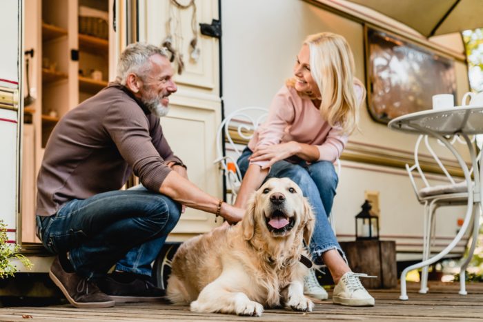 A heartwarming scene showing a mature couple sitting on their caravan porch with their Golden Retriever, illustrating the complexities of property division in unmarried separations. The man wears a brown jumper and jeans while the woman is in a pink sweater, both smiling while petting their dog, representing shared assets that may need consideration during separation.