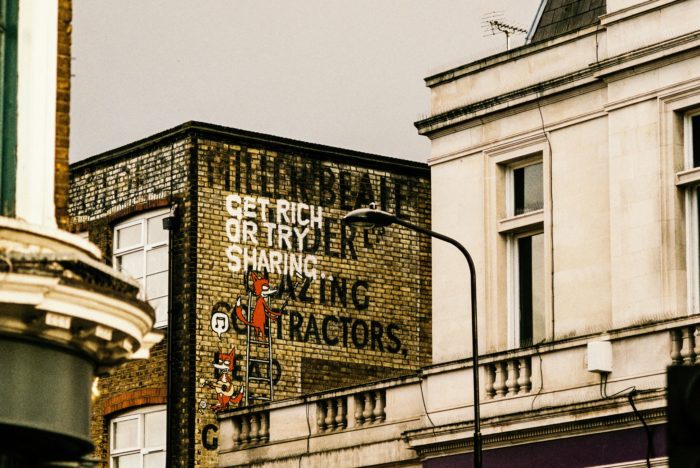 Urban street scene showing a brick building with graffiti that reads "Get rich or try sharing" alongside an illustration of a fox, used to illustrate the concepts of pension sharing and financial settlement.