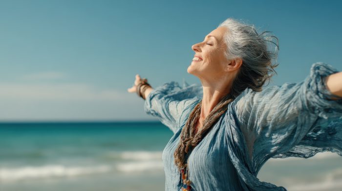 Menodivorce – a woman with grey hair enjoying freedom on a beach with arms outstretched